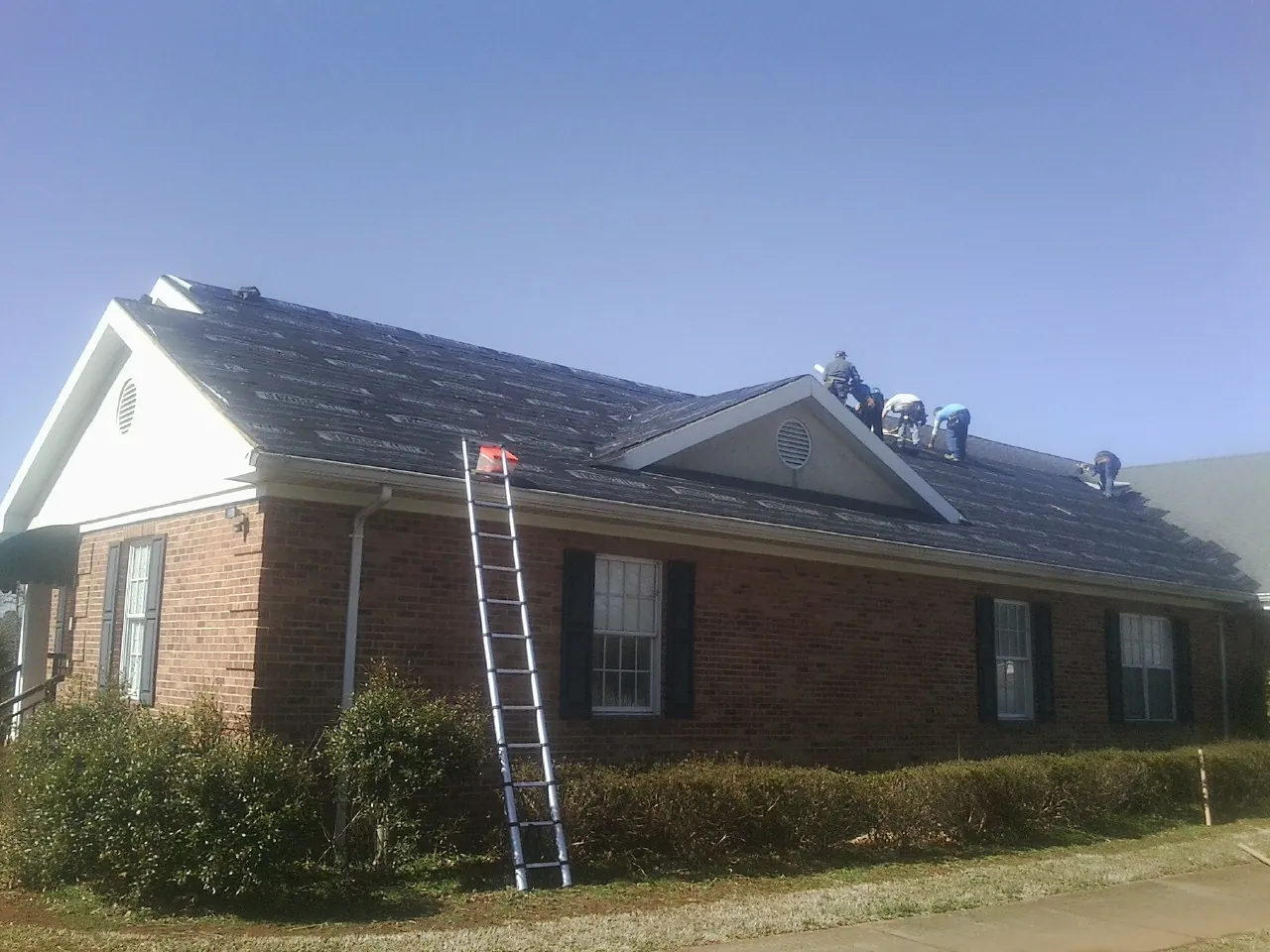 Crew tearing shingles off a brick ranch roof with a ladder set — Emergency Roof Repair work by our crew in Myrtle Point