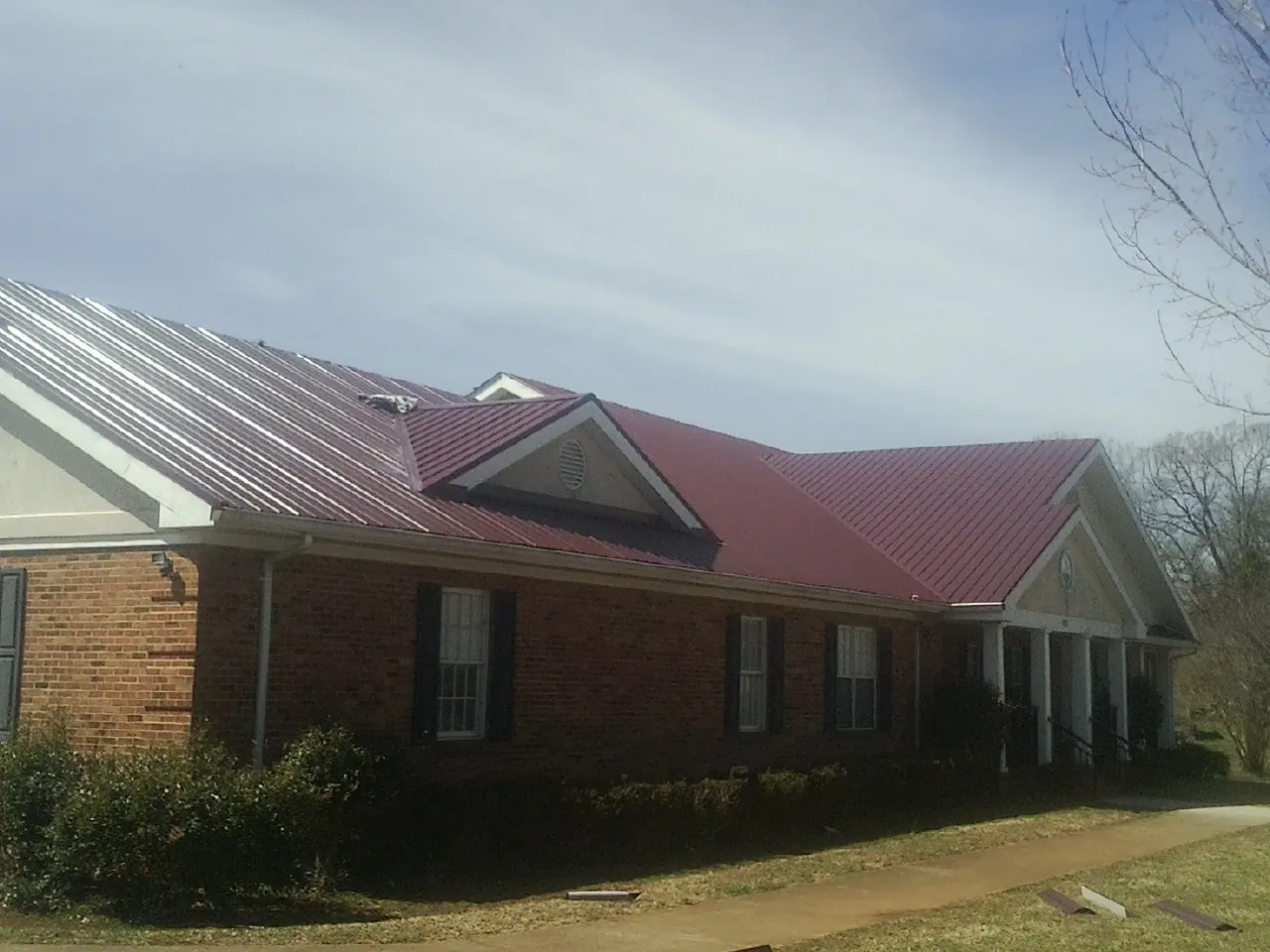 Red metal roof with gabled entries on a long brick building, from a Hail Damage Roof Repair job in Myrtle Point
