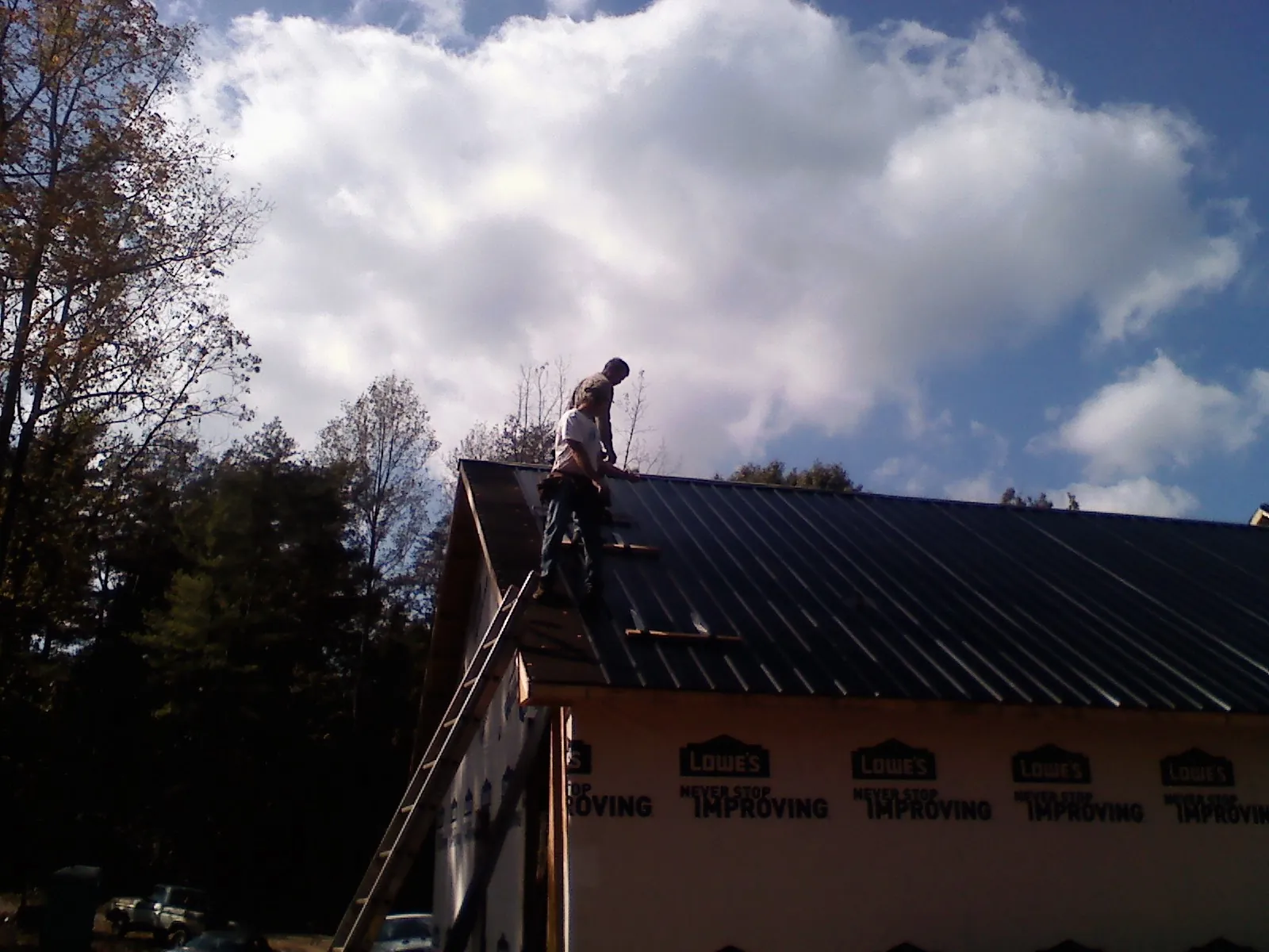 Roofer fastening dark metal panels high against a cloudy sky, from a Roof Inspection job in Myrtle Point