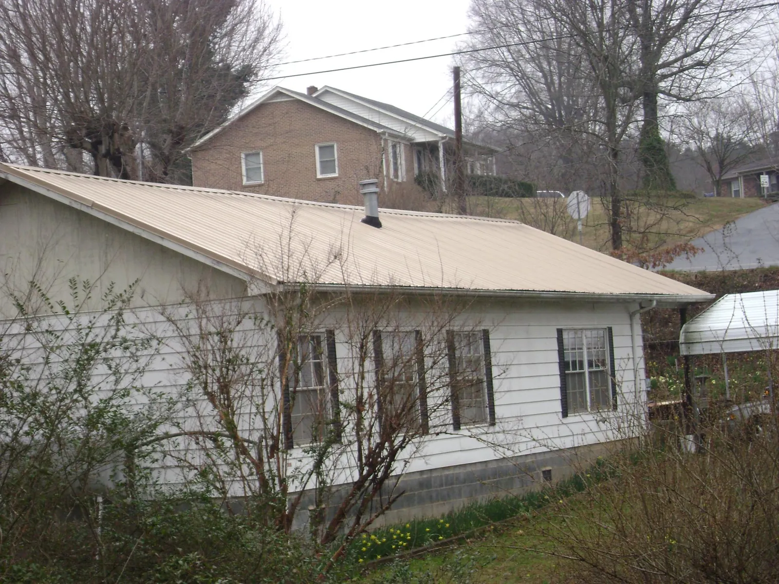 Tan metal roof on a white sided house set into a hillside — Commercial Roofing by Roofing Brothers in Myrtle Point