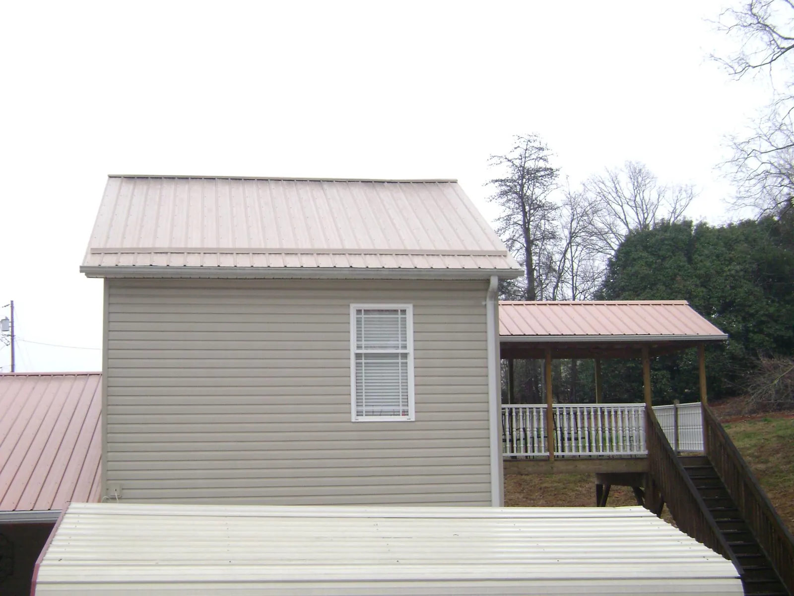 Tan metal roofs on a two story addition and attached porch, from a Roof Replacement job in Myrtle Point